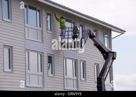 La peinture de l'homme en haut d'un bâtiment résidentiel, en travaillant à partir d'une grue hydraulique, plate-forme surélevée. Pays de Galles, Royaume-Uni Banque D'Images