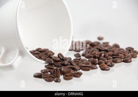 Une tasse de café blanc qui a baissé au cours des grains de café avec spilling out Banque D'Images