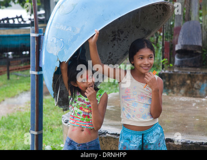 Deux filles timides à partir d'un abri de la pluie de douche dans une cabine téléphonique dans le couvercle de la météo d'Pacoval village, l'Amazonie, Brésil Banque D'Images