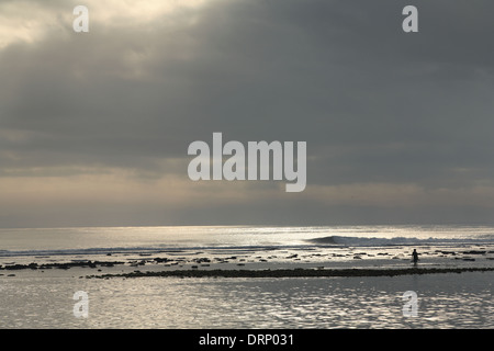 Matin spectaculaire silhouette d'un pêcheur à marcher le long du littoral de l'océan rocheux Bali, Indonésie - 05 novembre 2005 Banque D'Images