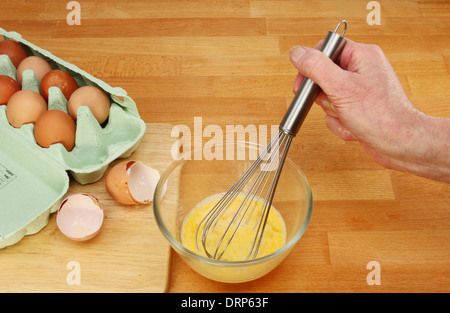 Main tenant un fouet, battre les oeufs dans un bol en verre sur un plan de travail de cuisine Banque D'Images