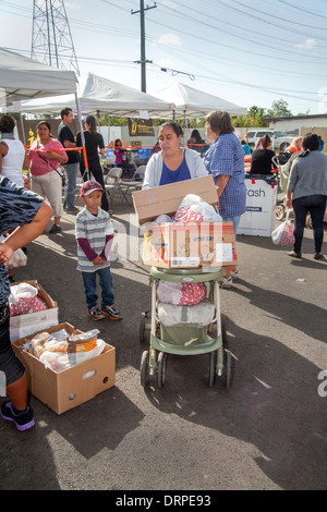 Une femme au foyer hispanique et ses enfants utiliser une poussette de bébé pour transporter de lourdes boîtes de dons en nourriture à partir d'un site de bienfaisance dans un taudis de Stanton, CA. Banque D'Images