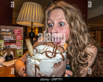 Une adolescente, tirant une drôle de visage, à propos de manger un très gros sundae dans un restaurant. Banque D'Images