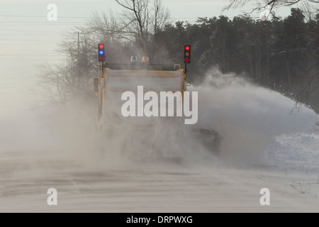 Un chasse-neige jaune efface une route dans le blizzard de vent que la neige a couvert la route créant de grandes dérives Banque D'Images