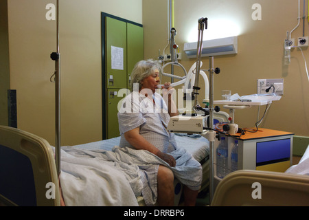 Patient à l'aide de la pompe d'aspiration de mucosités automatique alors qu'il était assis dans un lit d'hôpital Banque D'Images