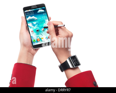 Femme portant Samsung Galaxy Gear watch et à l'aide du smartphone Galaxy Note III isolé sur fond blanc Banque D'Images