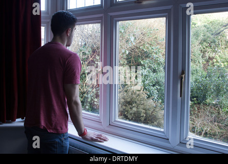 Jeune homme à l'intérieur à travers une fenêtre, plus d'épaule. Banque D'Images