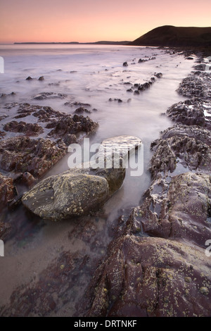 Les roches déchiquetées étant couverts par la marée montante au coucher du soleil sur la plage de Tenby, Pembrokeshire, Pays de Galles, Royaume-Uni Banque D'Images