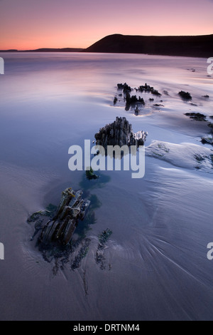 Les roches déchiquetées qui sort du sable à marée basse après le coucher du soleil sur la plage de Tenby, Pembrokeshire, Pays de Galles, Royaume-Uni Banque D'Images