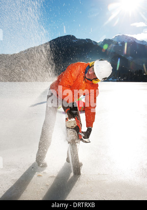 Un homme traverse un lac gelé avec une tronçonneuse pour récolter des blocs pour un concours de sculptures de glace. Whistler, BC, Canada Banque D'Images