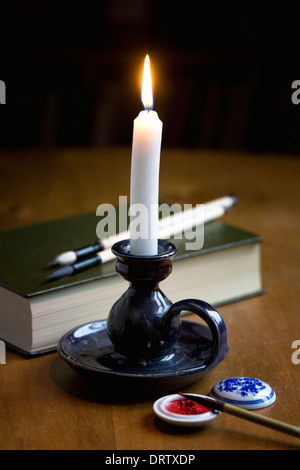 Une bougie blanche, calligraphie et un livre vert dans une pièce sombre. Banque D'Images