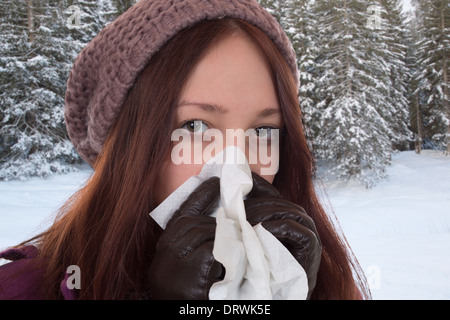 Jeune femme avec un tissu ayant un virus du rhume et de la grippe en éternuant outdoors Banque D'Images