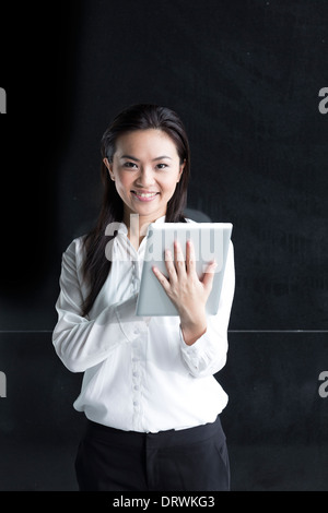 Femme chinoise avec un ordinateur tablette. Asian business woman using digital tablet computer, appuyé contre un mur noir. Banque D'Images