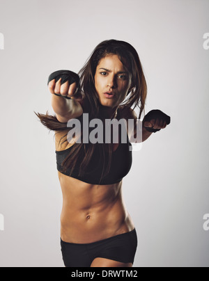 La jeune femme pratiquant la boxe. Middle punch jetant vers la caméra à l'arrière-plan gris Banque D'Images