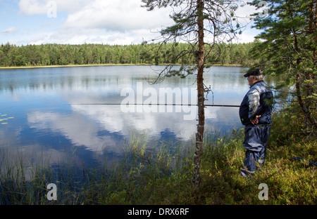 Homme âgé qui pêche dans un lac forestier à été, Finlande Banque D'Images