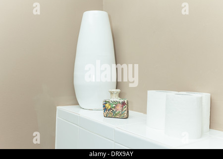 Vase de fleurs blanches et des rouleaux de papier de toilette sur le livre blanc du cabinet. Banque D'Images