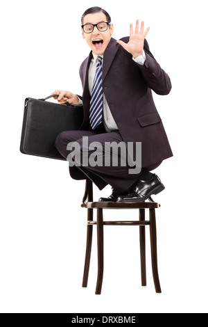 Terrifié businessman holding briefcase debout sur une chaise et crier Banque D'Images