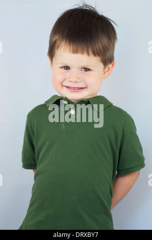 Cute little boy with main derrière son dos et un grand sourire Banque D'Images