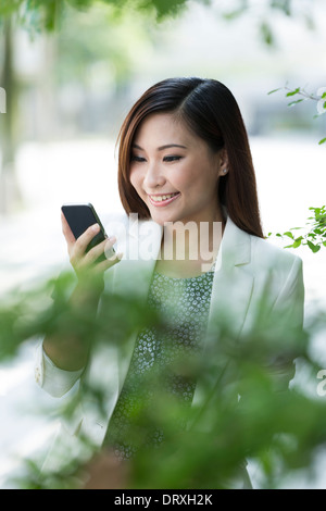 Asian Businesswoman en utilisant un téléphone intelligent. Happy smiling Chinese business woman walking in street en utilisant les téléphones cellulaires. Banque D'Images