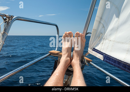 L'homme ses pieds reposant sur un voilier. Banque D'Images