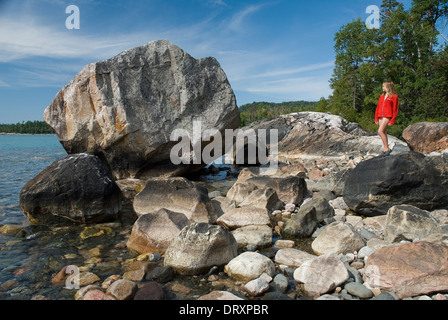 Jeune fille se tient sur de grosses roches sur une rive du lac. Banque D'Images