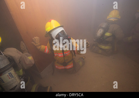 Les étudiants de l'école secondaire académie du feu ramper dans la maison remplie de fumée à piégé des occupants 'lors d'un exercice d'entraînement Banque D'Images