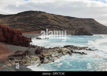 Les vagues déferlent sur la plage de gravier noir entouré de roches de couleur près d'El Golfo, Lanzarote, îles Canaries, Espagne Banque D'Images