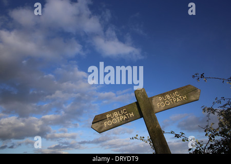 Un vieux sentier public en bois panneau, avec des flèches pointant dans deux sens, contre un ciel bleu avec des nuages. Banque D'Images