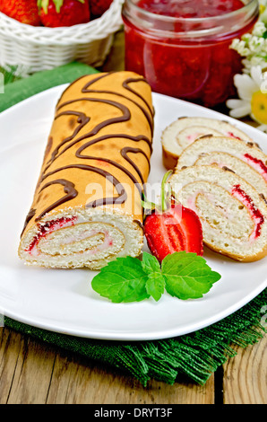 Roulade de biscuit à la crème et de la confiture, pot de confiture, napperon, fraises, menthe sur fond de planches en bois Banque D'Images