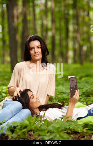 Fille avec la tête sur les genoux de sa mère la lecture d'un livre à un pique-nique dans une forêt Banque D'Images