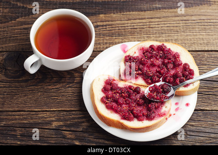 Le pain blanc avec confiture de framboises et une tasse de thé sur la table Banque D'Images