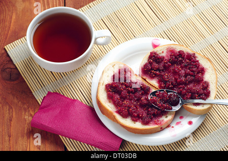 Le pain avec la confiture de framboises dans une assiette et tasse de thé Banque D'Images