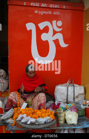 Femme hindoue faisant une guirlande de fleurs avec œillets. Au-dessus d'elle, le symbole hindou Om (Inde) Banque D'Images