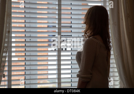 Silhouette de femme portant une robe de chambre à la recherche d'une fenêtre. Plus de retour de l'épaule/Vue de côté. Banque D'Images