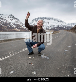 Le géophysicien dans la route essayant d'obtenir l'attention des oiseaux volant au-dessus, l'Ouest, l'Islande, Sugandafjordur Banque D'Images
