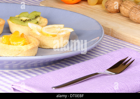 Assortiment de mini tartelettes aux fruits sur une plaque en céramique avec fruit dans l'arrière-plan. Focus sélectif. Banque D'Images