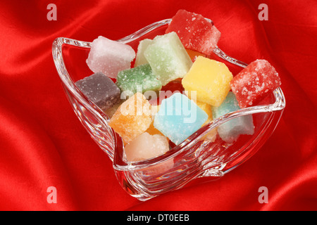 Bonbons colorés fondant mélangés dans une tasse en verre sur un fond rouge. Soft focus sélectif. Banque D'Images