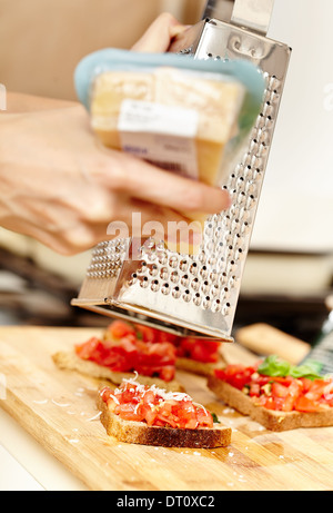 Libre de Cook's mains râper un morceau de tomate au parmesan bruschettas, selective focus Banque D'Images