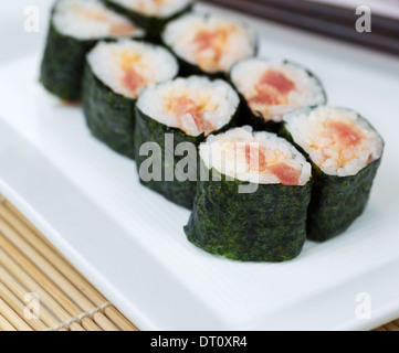 Photo gros plan de thon épicé sushi roll en plaque blanche et baguettes en arrière-plan avec des panneaux de nattes de bambou en dessous Banque D'Images