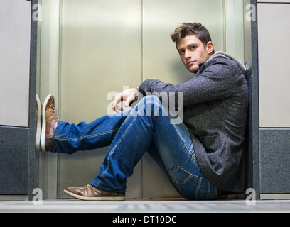 Beau jeune homme assis en face de l'ascenseur) Portes, looking at camera Banque D'Images