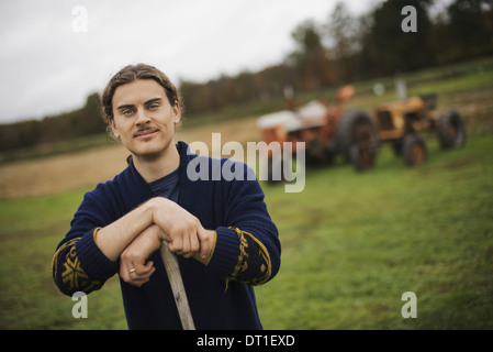 Agriculteur biologique au travail un homme s'appuyant sur une binette à jardin un tracteur à l'arrière-plan Banque D'Images
