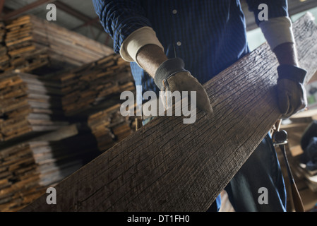 Un tas de sciages recyclés des planches de bois dans un parc de séchage un homme portant une grande planche de bois Banque D'Images