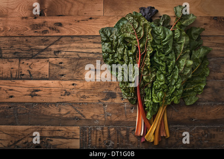 Groupe des feuilles de bette à carde rouge et orange avec des tiges de couleur des légumes biologiques fraîchement cueilli et mis sur une planche en bois Banque D'Images