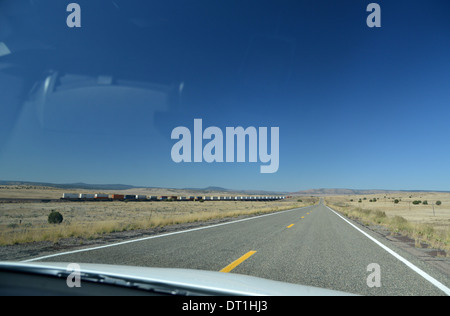 La route 66, Arizona, USA. Longtemps, seul, route droite et un train de marchandises énorme disparaître dans la distance à travers le pare-brise Banque D'Images