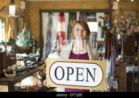 Une femme debout dans un magasin d'antiquités brandissait une inscription affiche des marchandises tout autour d'elle Banque D'Images Une femme debout dans un magasin d'antiquités brandissait une inscription affiche des marchandises tout autour d'elle Banque D'Images