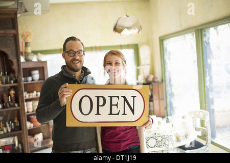 Deux personnes debout dans un magasin rempli d'objets antiques un couple d'exploiter une entreprise tenant un grand panneau disant OUVRIR Banque D'Images