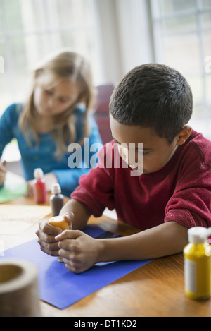 Les enfants dans une maison de Famille Deux enfants assis à la table à l'aide de peinture et de papier pour créer des décorations Banque D'Images