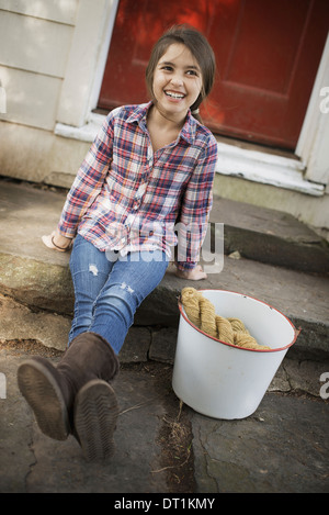 Une fille assise sur une étape avec un grand seau en fer et des gants Banque D'Images