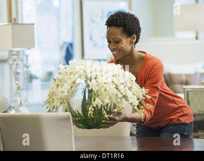 Femme plaçant vase de fleurs sur table Banque D'Images