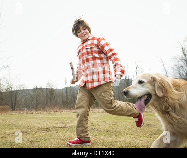 Un jeune garçon à l'extérieur par une journée d'hiver tenant un bâton et fonctionnant avec un golden retriever dog Banque D'Images